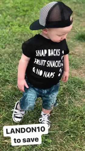 a small baby is standing in the grass wearing an army shirt