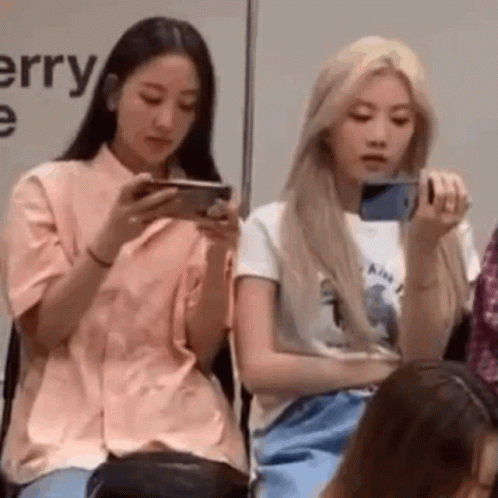 two girls sitting side by side using cell phones