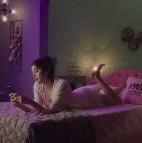 a lady laying on her bed while looking at her cell phone