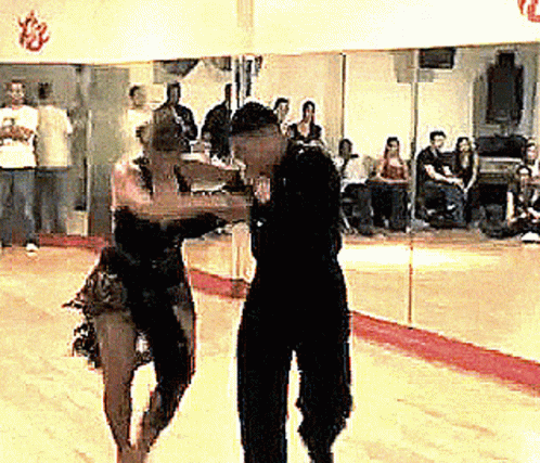 two people in a dance studio with a crowd looking at them