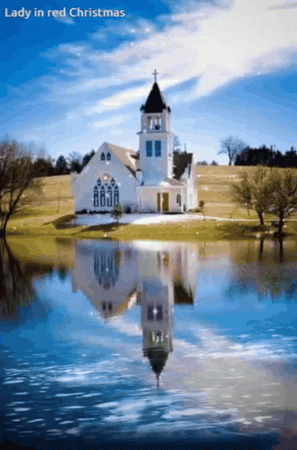 the church has a tall steeple and has its reflection in the water