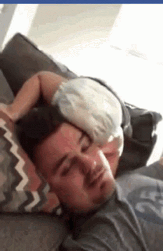 a man is taking a nap on his couch with a stuffed animal on top of his head