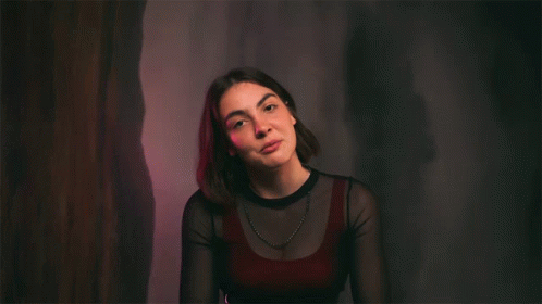 a girl sitting in a dark room with her hand on her stomach