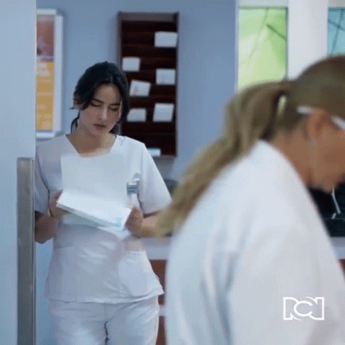 a woman wearing scrubs and making a face while walking through a hallway