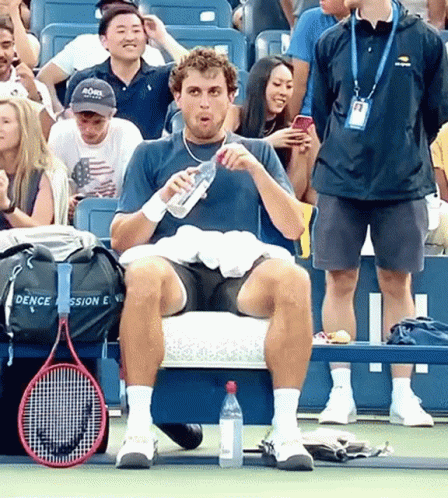 man sitting on bench in front of audience with tennis racket and bottle