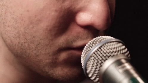 closeup of the face of a young man, wearing blue, holding a microphone to his ear