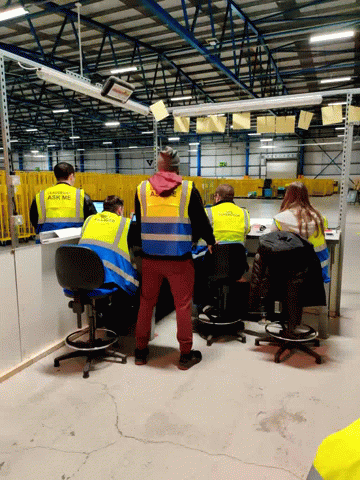 a group of workers sitting around desks wearing safety vests