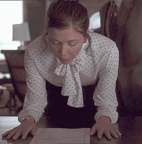 a woman wearing a polka dotted blouse looking at an open book