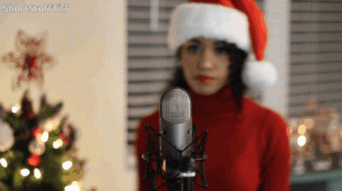 a person in a santa claus hat with blue makeup and a microphone in front of a window