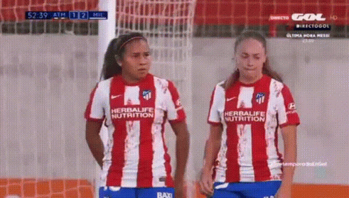 two girls in uniforms standing next to each other on a soccer field