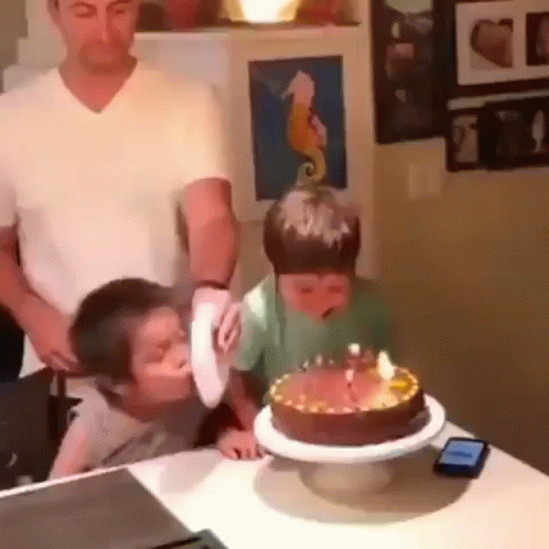 two small boys are playing with their father on the birthday cake