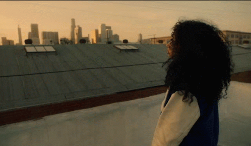 a girl with long dark curly hair walking on the rooftop