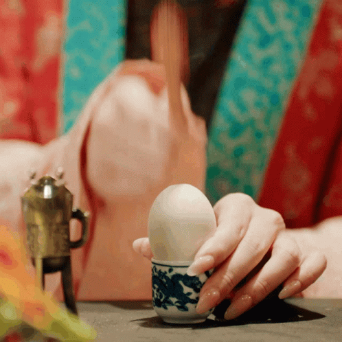 a hand is holding a plastic egg, in front of an empty cup