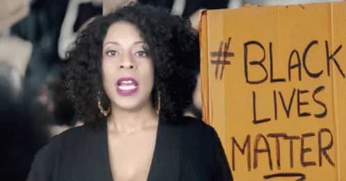 a woman standing behind a sign with black lives matter written on it