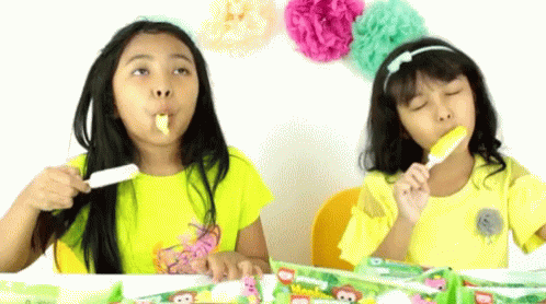two girls sitting at a table brushing their teeth