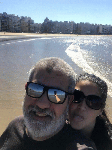 a couple in sunglasses taking a selfie with a city beach