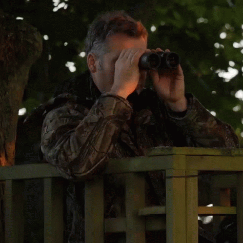 a man in camouflage holding a binoculars looks through it