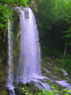 a large waterfall surrounded by green trees and rocks