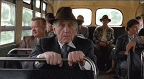 a old man driving on a bus with men wearing hats