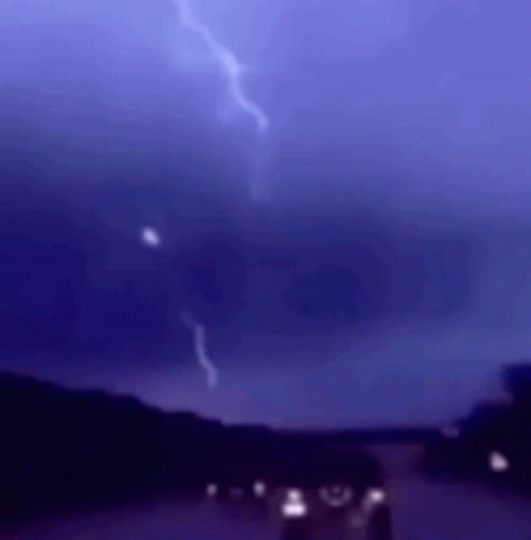 a couple of cars parked under a lightning storm