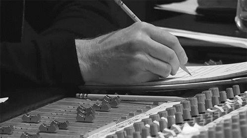 a person writes in a notebook at a table full of recording equipment