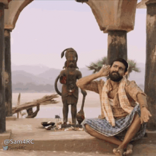 an indian man is sitting in front of two statues