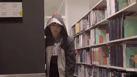 man with hoodie on in front of stacks of books