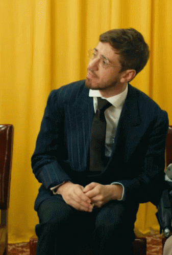 man in suit sitting down with his hands folded