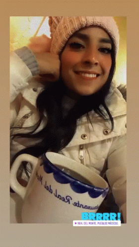a woman in winter clothing holding a mug and smiling