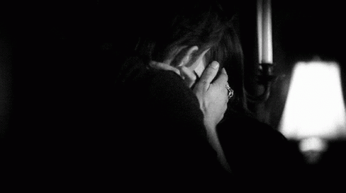 a woman in a dark room holding her hand to her face