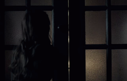 a girl stands next to a dark lit door