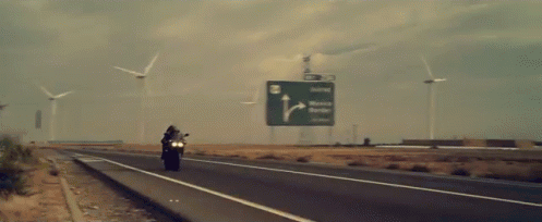 a motorcycle is driving down a road with windmills