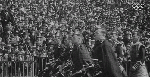 two men with their instruments are marching while an olympic crowd watches