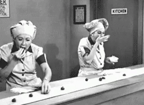 two women wearing kitchen aprons on top of a counter