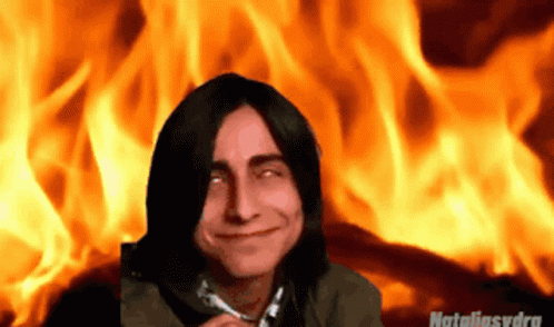 a man with long hair standing in front of a fire background