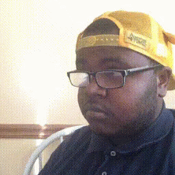 a black man wearing glasses, a blue hat and a brown shirt