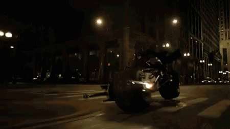 a black motorcycle driving down a street in the dark