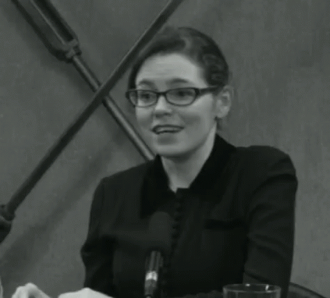 a woman in glasses is smiling while sitting in a conference room