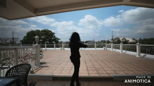 woman with long dark hair standing alone with arms raised facing an empty patio