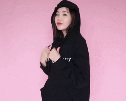 a woman posing in a hooded sweatshirt and holding a cell phone