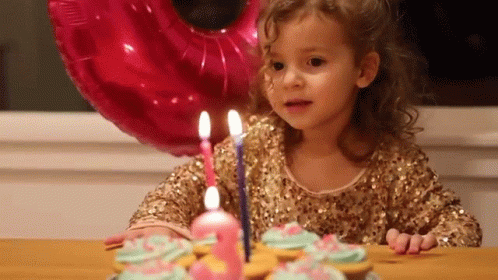 a little girl sits at a table in front of a cake with candles on it