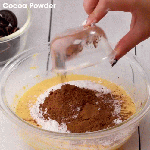 someone adding blue powder to blue and white powder in a glass bowl