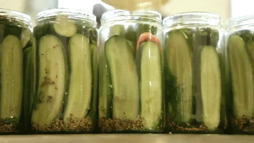 a row of jars full of pickles with spoon