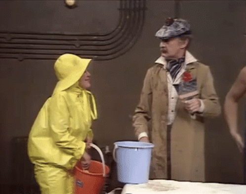 two men in blue rain suits and one in gray coat hold a bucket while standing near a train