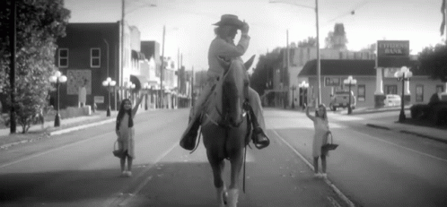 black and white pograph of two women riding horses on city street