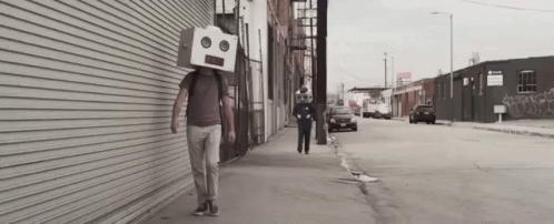 a person walking on the street while wearing a box head mask