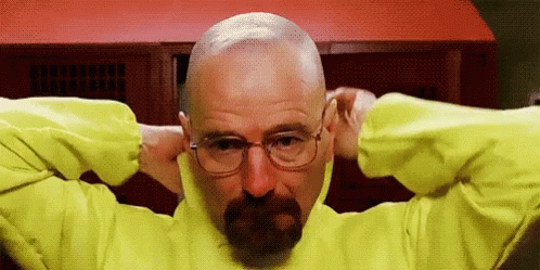 a bald man wearing glasses and blue sweater holding his head