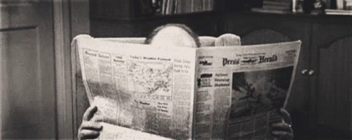 a woman sits in a chair and reads a newspaper
