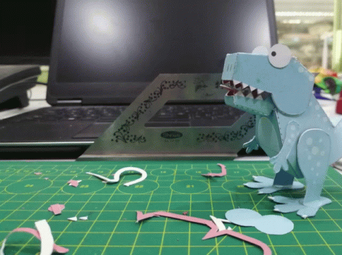 a dinosaur is making out of paper next to a computer