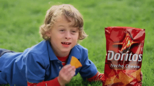 a  with blond hair lies down on the grass while holding a bag of donuts